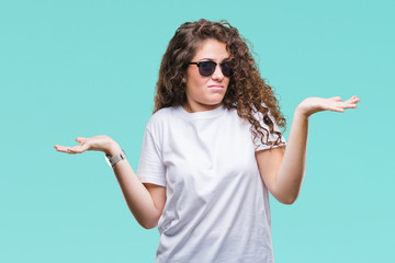 Beautiful brunette curly hair young girl wearing sunglasses over isolated background clueless and...