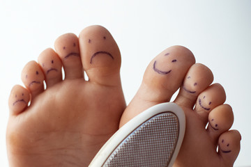 Female toes with painted smileys and a pedicure grater. Foot care concept.