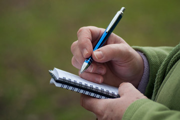 closeup of hand of woman writing on notebook in outdoor