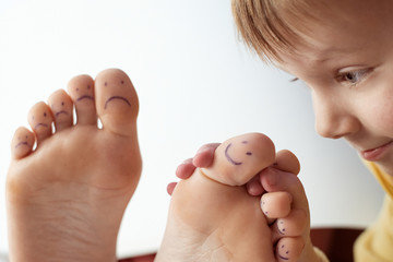 Female toes with painted smileys and baby. Foot care concept, pedicure.