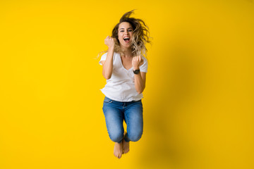 Beautiful young blonde woman jumping happy and celebrating with raised hands and open mouth over...