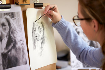 Rear View Of Female Teenage Artist Sitting At Easel Drawing Picture Of Dog From Photograph In...