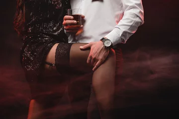 cropped view of erotic woman hugging man with glass of whiskey in red smoky room © LIGHTFIELD STUDIOS