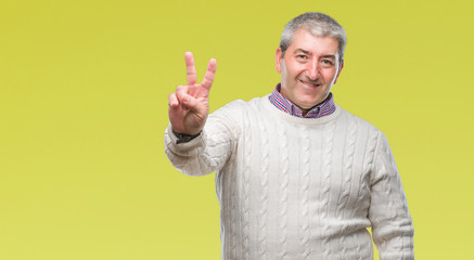 Fototapeta premium Handsome senior man wearing winter sweater over isolated background smiling with happy face winking at the camera doing victory sign. Number two.