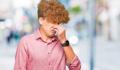 Young handsome business man with afro hair smelling something stinky and disgusting, intolerable...