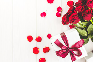 Red roses and gift box on white wooden table, top viewed