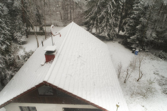 Snow-covered, roof, of a detached house in a forest with a snow-covered satellite antenna and pines at the edge.