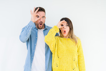 Young beautiful couple togheter over isolated background doing ok gesture shocked with surprised face, eye looking through fingers. Unbelieving expression.