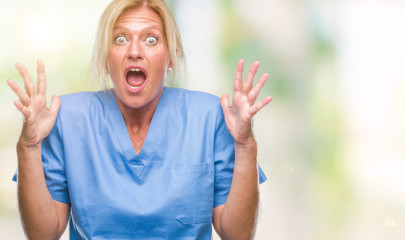 Middle age blonde woman wearing doctor nurse uniform over isolated background crazy and mad shouting and yelling with aggressive expression and arms raised. Frustration concept.