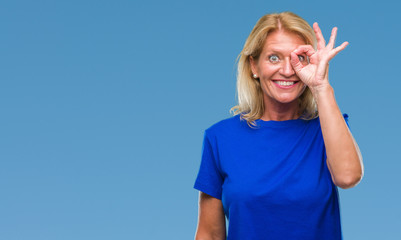 Fototapeta premium Middle age blonde woman over isolated background doing ok gesture with hand smiling, eye looking through fingers with happy face.