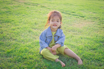 Fototapeta premium happy little girl sitting on green grass and playing in the park. soft focus.