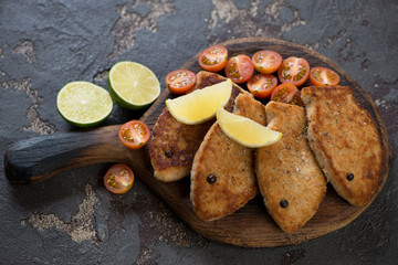 Fried fish cutlets made of pike on a rustic wooden serving board, studio shot on a brown stone background