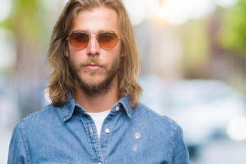 Young handsome man with long hair wearing sunglasses over isolated background with serious expression on face. Simple and natural looking at the camera.