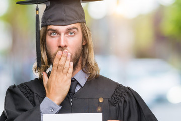Young handsome graduate man with long hair holding blank paper over isolated background cover mouth with hand shocked with shame for mistake, expression of fear, scared in silence, secret concept