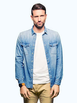 Handsome man with blue eyes and beard wearing denim jacket skeptic and nervous, frowning upset because of problem. Negative person.