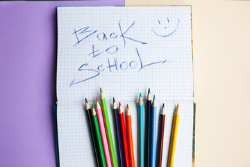 Color pencils lying on pastel purple and beige background. Squared notebook with back to school concept sign and smile. Colorful art studying and painting. Copy space place for postcard wish.