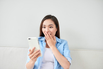 Excited woman reading text on a phone lying on a couch in the living room at home