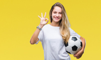 Young beautiful blonde woman holding soccer ball over isolated background doing ok sign with...