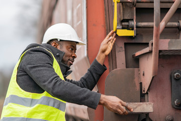 African American mechanic wearing safety equipment (helmet and jacket) checking gear train