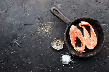 Fototapeta na wymiar Two steaks of pink salmon of the salmon family, wild sea fish. Healthy food for the whole family. Top view. On a dark background in a cast iron skillet before baking with salt and pepper.