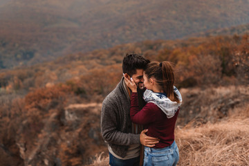 Couple standing at viewpoint and kissing. In background forest, autumn time.