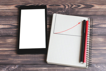  notepad on which the graph with the red arrow of profit growth is drawn and the laptop lie on the table. On the notepad are two markers red and black.