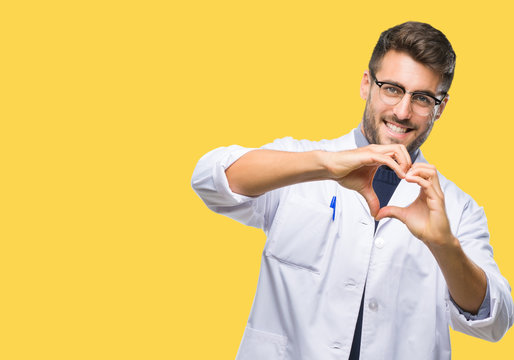 Young handsome man wearing doctor, scientis coat over isolated background smiling in love showing heart symbol and shape with hands. Romantic concept.