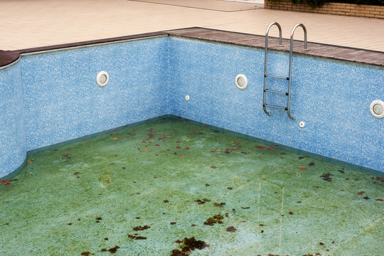 Dirty swimming pool without water with metal staircase