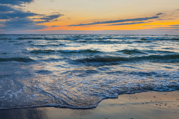 Low waves on Baltic sea at sunset. Cosy flat sandy beach.