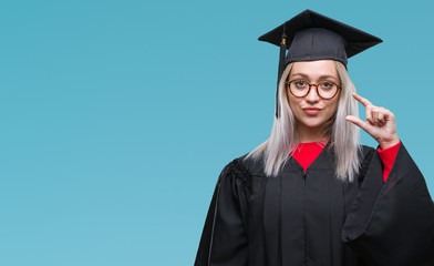 Young blonde woman wearing graduate uniform over isolated background smiling and confident gesturing with hand doing size sign with fingers while looking and the camera. Measure concept.