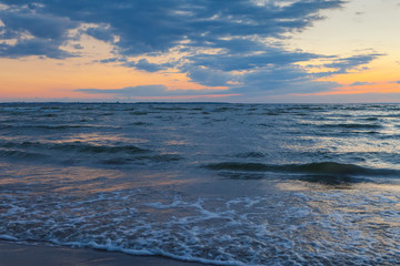 Low waves on Baltic sea at sunset. Cosy flat sandy beach.