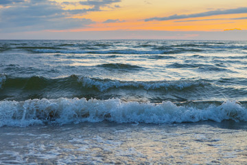 Fototapeta na wymiar Low waves on Baltic sea at sunset. Cosy flat sandy beach.