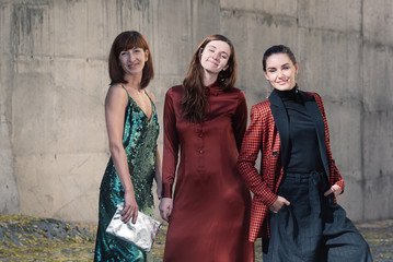 Street style Fashion portrait three charming women. Brown and green dress, Black, tile red jacket, silver bag. Summer Spring Fall collection beautiful look. Togetherness, friendship, party concept