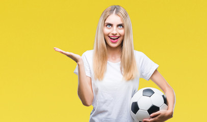 Young beautiful blonde woman holding soccer ball over isolated background very happy and excited, winner expression celebrating victory screaming with big smile and raised hands