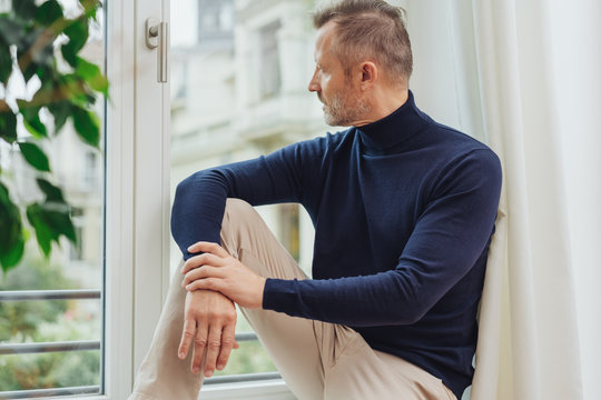 Man in blue sweater sitting on window sill