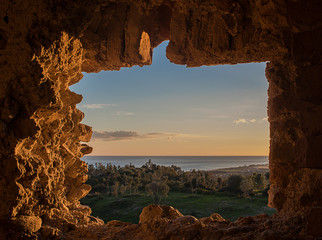 Window in Stone Wall. Hills with trees and sea in background. Sunset orange and blue sky