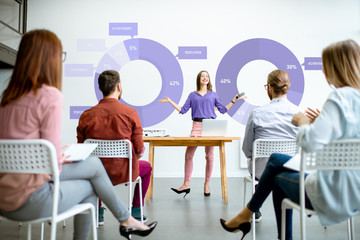 Young woman speaker reporting to the audience during the meeting in the conference room with charts...