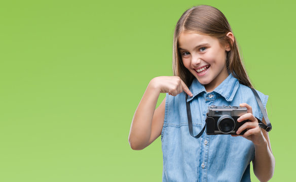 Young beautiful girl taking photos using vintage camera over isolated background with surprise face pointing finger to himself