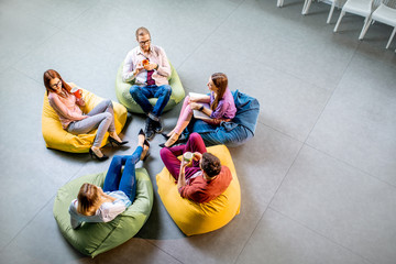 Group of a young coworkers sitting together on the colorful poufs resting during the coffee break...