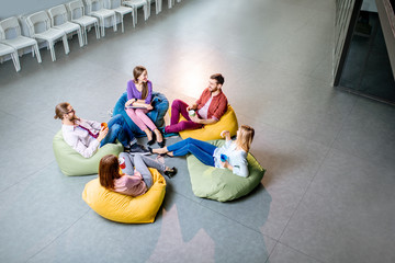 Group of a young coworkers sitting together on the colorful poufs resting during the coffee break in the office, view from above