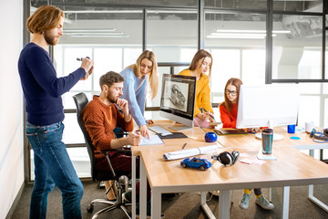 Group of young creative coworkers designing a car model at the working place with computers in the...