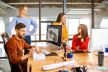 Group of young creative coworkers designing a car model at the working place with computers in the...