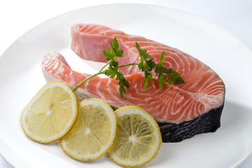 Salmon steak with a sprig of parsley and three lemon slices on a white plate.