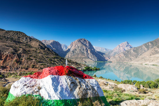 Iskanderkul Lake with a large rock painted in the colours of the Tajikistan flag in the foreground, Fan Mountains, Tajikistan