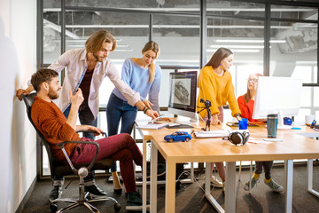 Group of young creative coworkers designing a car model at the working place with computers in the...
