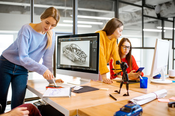 Group of young creative coworkers designing a car model at the working place with computers in the...