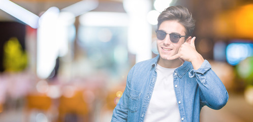 Young handsome man wearing sunglasses over isolated background smiling doing phone gesture with hand and fingers like talking on the telephone. Communicating concepts.
