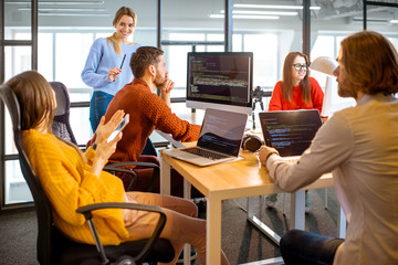 Team of a young programmers dressed casually working on computer code sitting in the modern office...