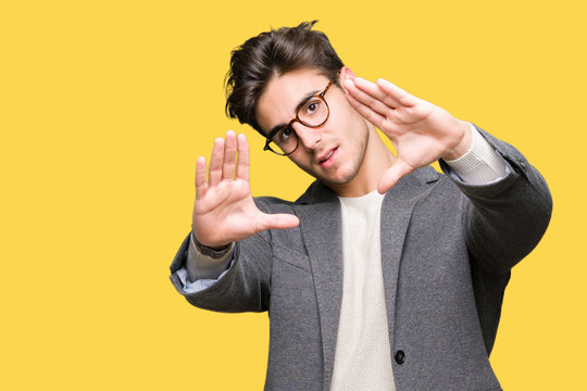 Young business man wearing glasses over isolated background Smiling doing frame using hands palms and fingers, camera perspective
