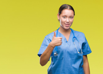 Young caucasian doctor woman wearing medical uniform over isolated background doing happy thumbs up gesture with hand. Approving expression looking at the camera with showing success.